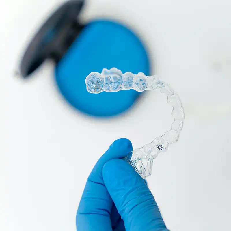 Photo of clear aligners, which are a thin, plastic mold of teeth used to gradually correct tooth alignment. The aligners are being held up to emphasize that they are thin and subtle in appearance.